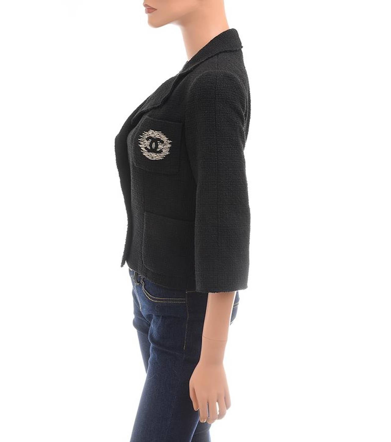 Chanel black boucle cropped jacket with notch collar and lapels, breast pocket with large silver CC embroidered applique, front button closure in double breasted style, 3/4 sleeves, and signature CC and camellia silk lining with weighted chain at