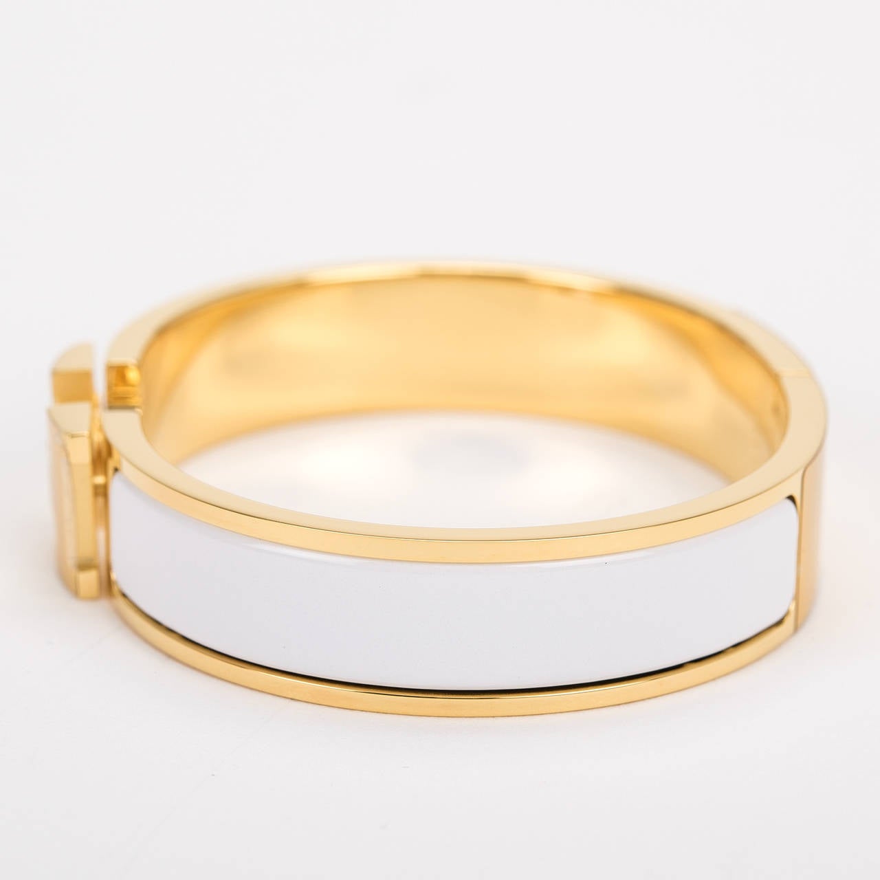 Hermes narrow Clic Clac H bracelet in White enamel with gold plated hardware in size PM.

Hermes is renowned for its enamel and leather bracelets. Hermes printed enamel bangles, enamel Clic Clac H bracelets, and leather/exotic Collier de Chien