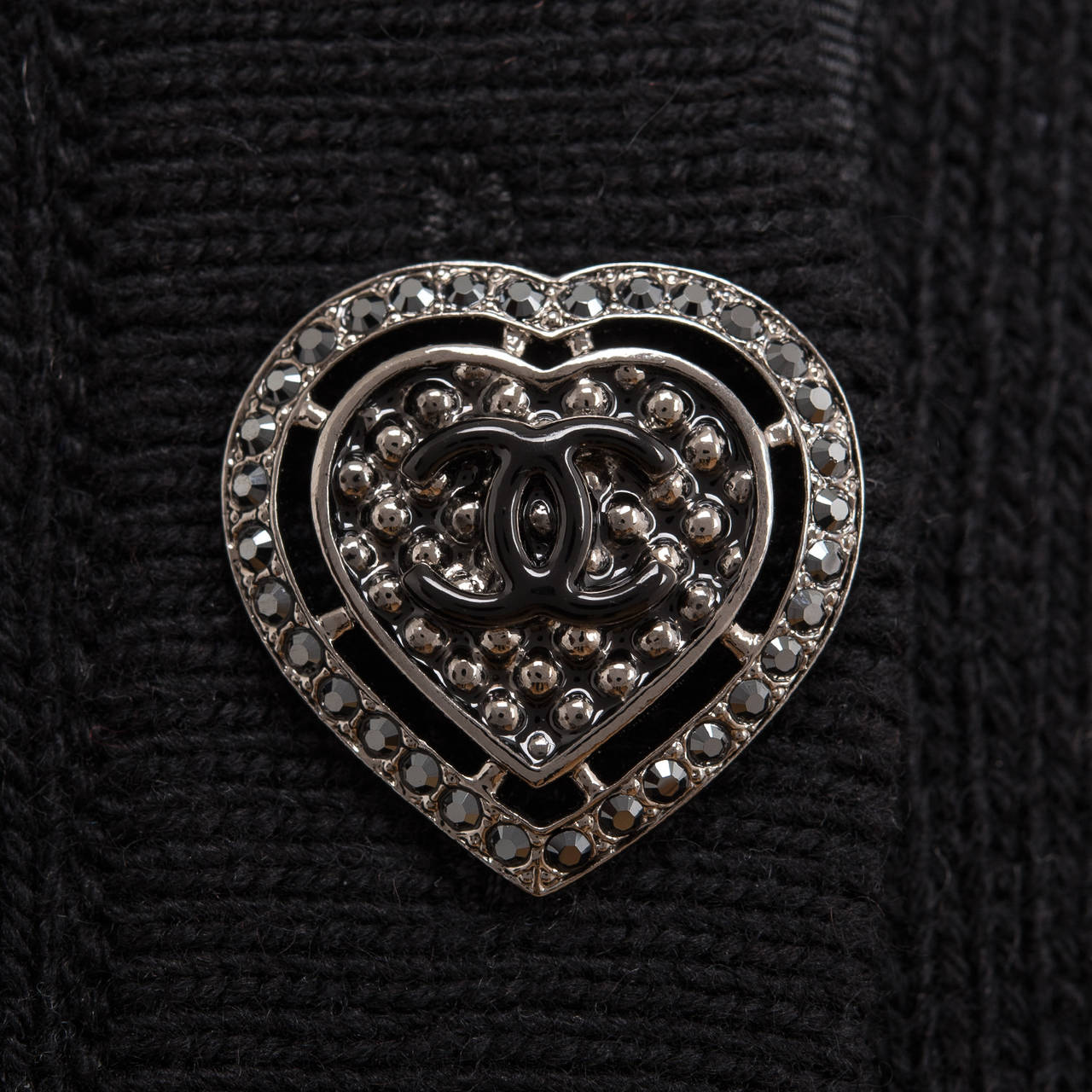 Chanel black cashmere sweater coat with round neckline, six CC-stamped jewel and enamel silver tone heart buttons, hip level patch pockets, bracelet sleeves and vertical ribbed trimming  at pockets, cuff, and bottom.
 
Fabric: 100% cashmere
