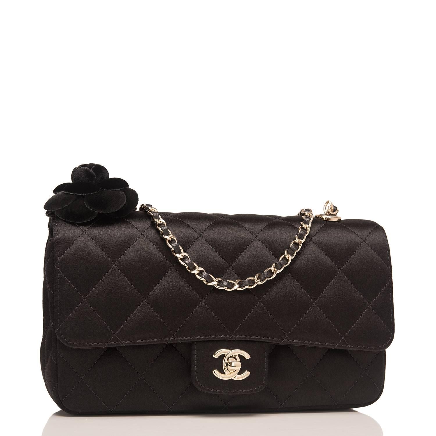 Chanel Camellia Mini flap bag of black satin with light gold tone hardware.

This bag features a front flap with CC turnlock closure, a black velvet camellia flower charm, and an interwoven light gold tone chain link and black leather