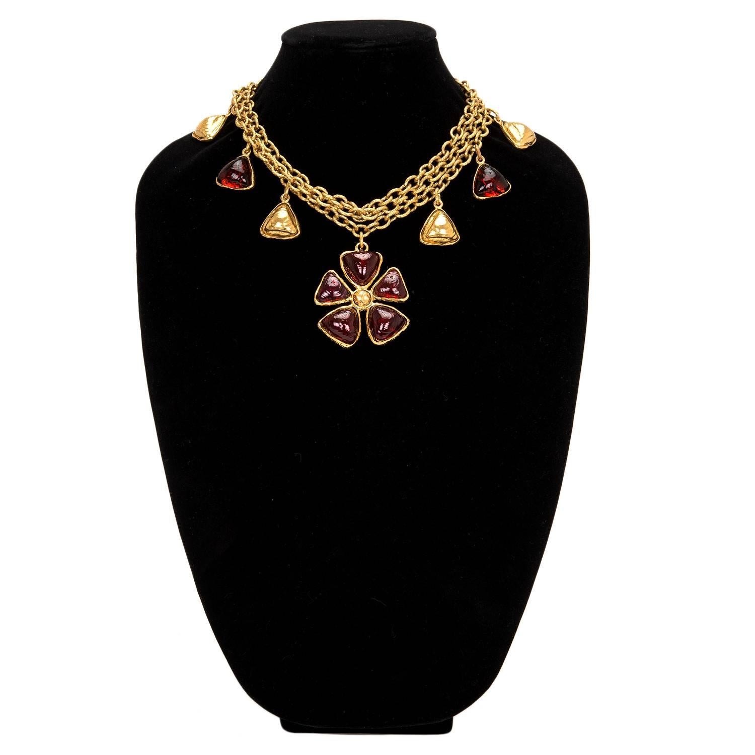 Chanel layered gold tone chain link necklace with large ruby gripoix flower pendant, eight dangling gripoix and gold tone triangular charms and two gripoix charms at closure.

Collection: circa 1970's

Condition: Vintage; excellent

Accompaned