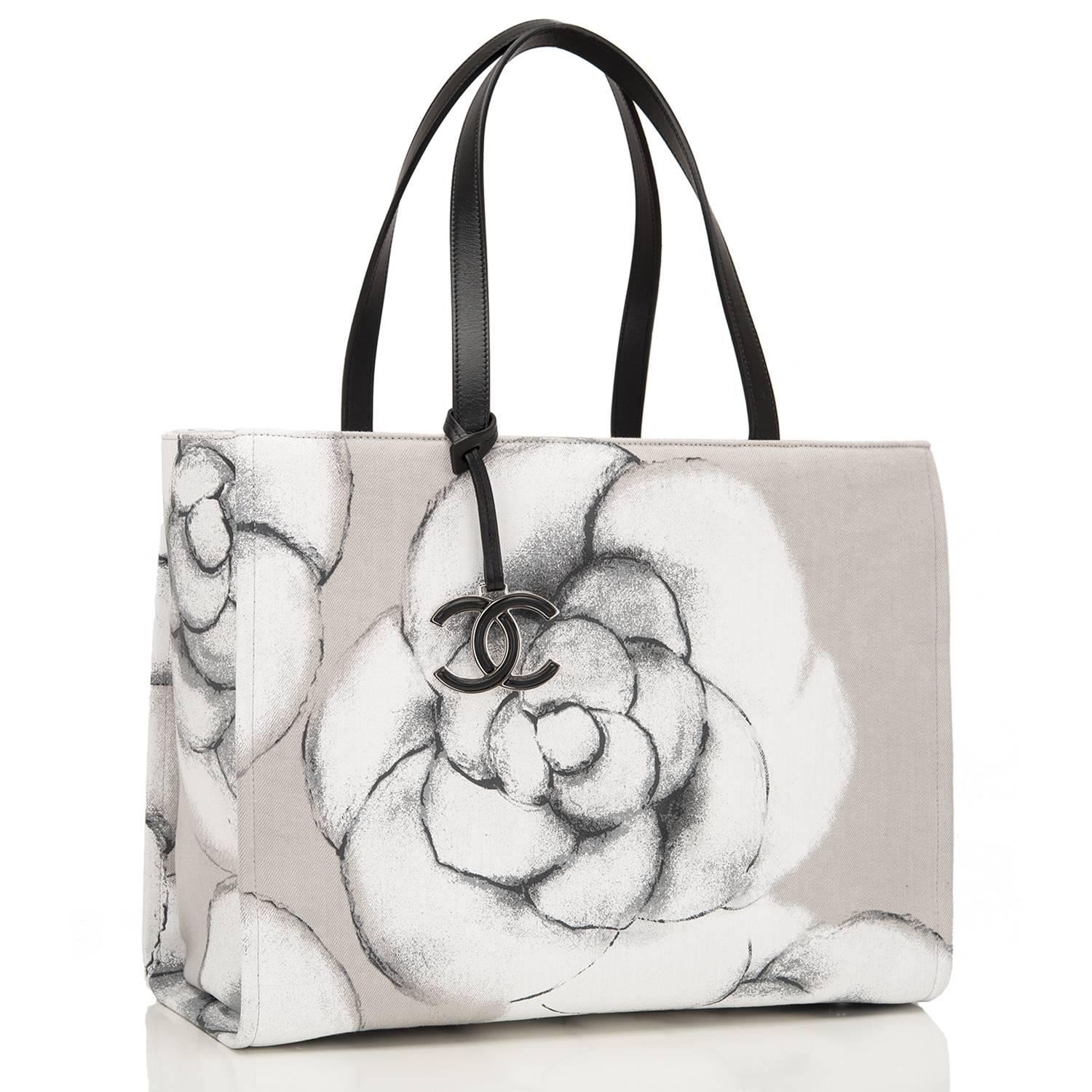 Chanel canvas camellia shopping tote with black leather accents and silver and black tone hardware. 

This limited edition bag has flat black handles, a dangling silver and black tone CC metal charm and four feet at bottom. 

The interior is of