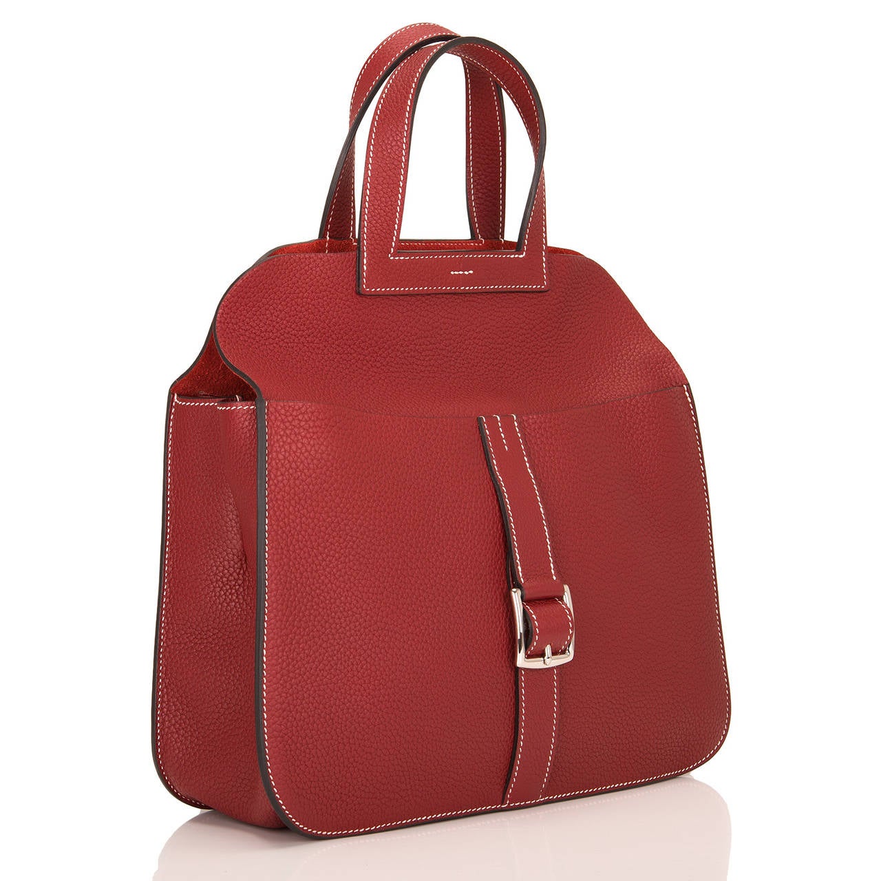 This Hermes Rouge H Halzan bag is made of clemence leather with white contrast stitching, front buckle closure, two front pockets, two back pockets, and double flat leather handles and attachable single flat leather shoulder strap

The interior is