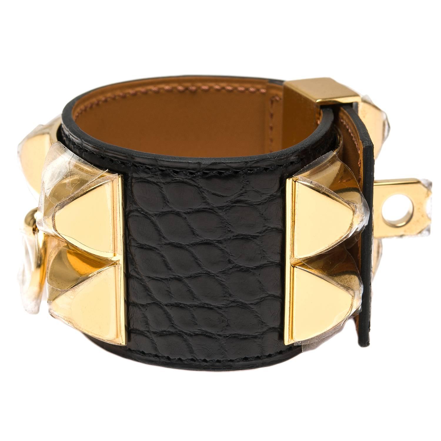 Hermes Collier de Chien (CDC) bracelet in black matte alligator with gold plated hardware in size Small.

This adjustable bracelet has a front gold plated plate of four gold pyramid studs and a center ring and a rear plate with four slots with a
