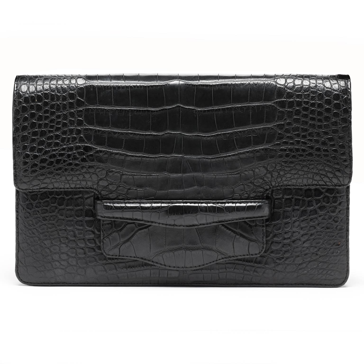 This matte black alligator clutch is fully lined in leather, with an inner zipper pocket. The adjustable alligator strap is joined to the bag with a set of gold sculpted hands on both sides. The strap can extend from 18