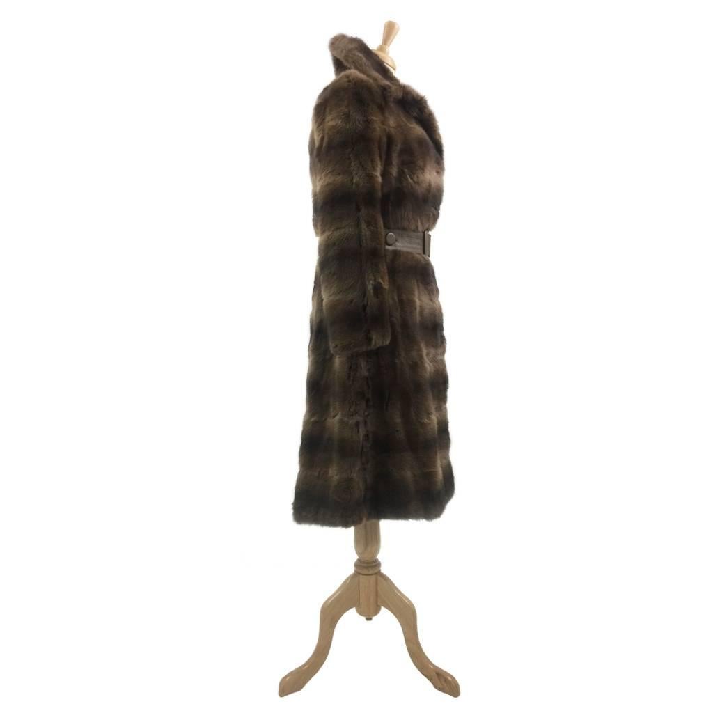 This soft fur vintage sample coat is styled in the classic 1970s trench coat silhouette.  The furs have been designed in horizontal bands and the waistband is leather with a buttoned belt. The colour of the leather is perfect 70’s olive