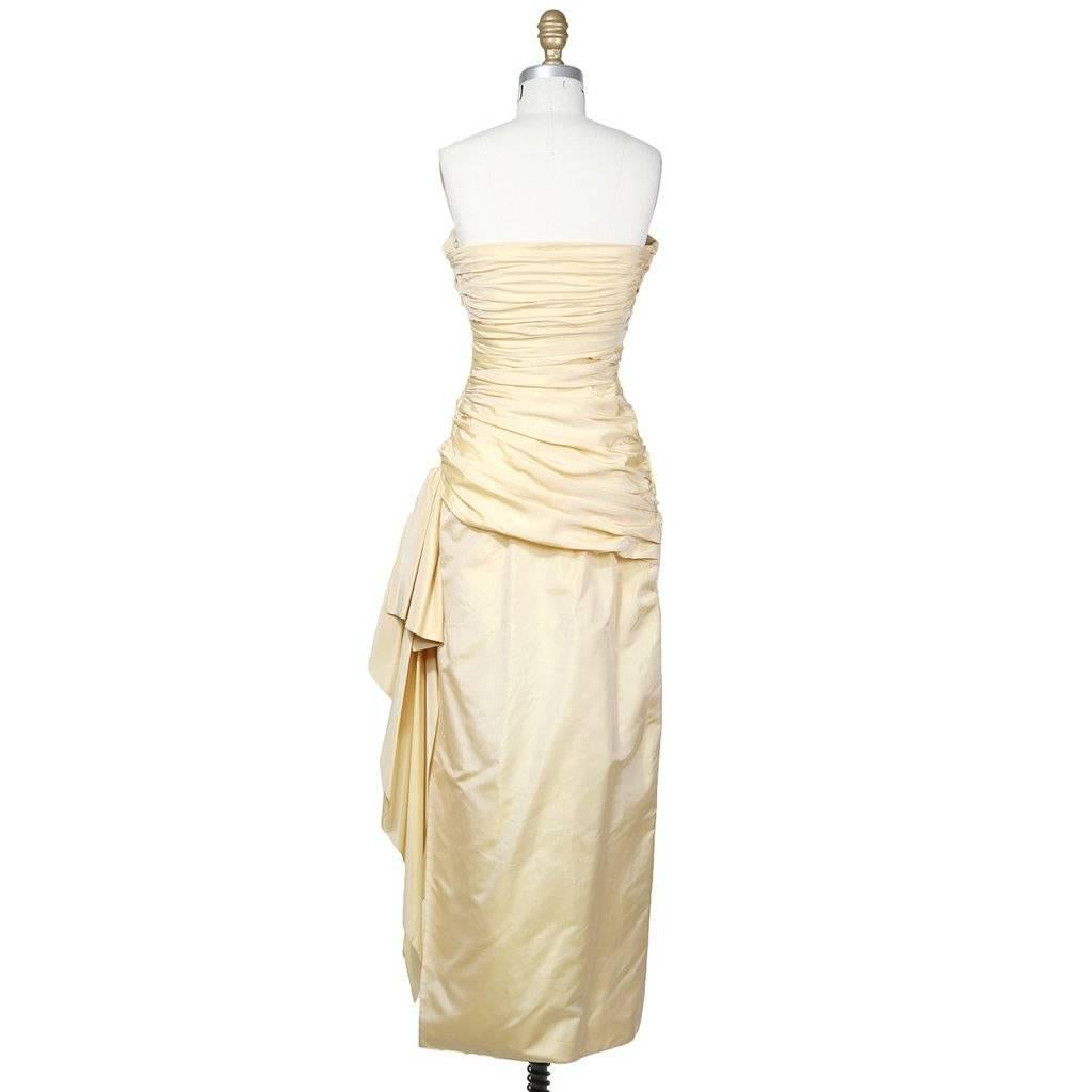 Details include side slit, sweetheart neckline with crossover fabric on bust, silk satin exterior, side sewn-bown attached to side with excess fabric over side slit, bodice gathered at the side seams around bodice down to the hips and draped skirt