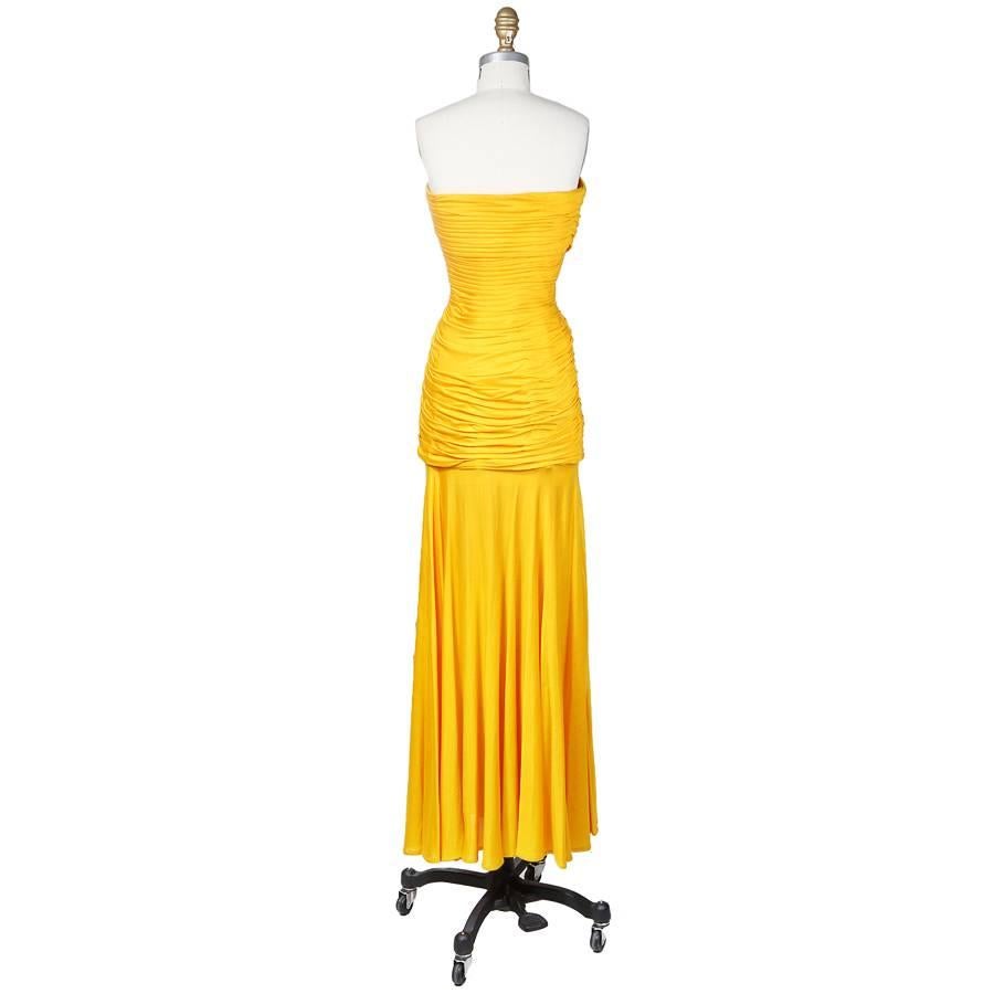 This is a strapless dress by Emmanuel Ungaro. It's made from a golden yellow silk jersey.  The fabric ruching around the center is delicately folded and includes two body conforming drapes over the bust.  Features a hidden side zipper with hook and