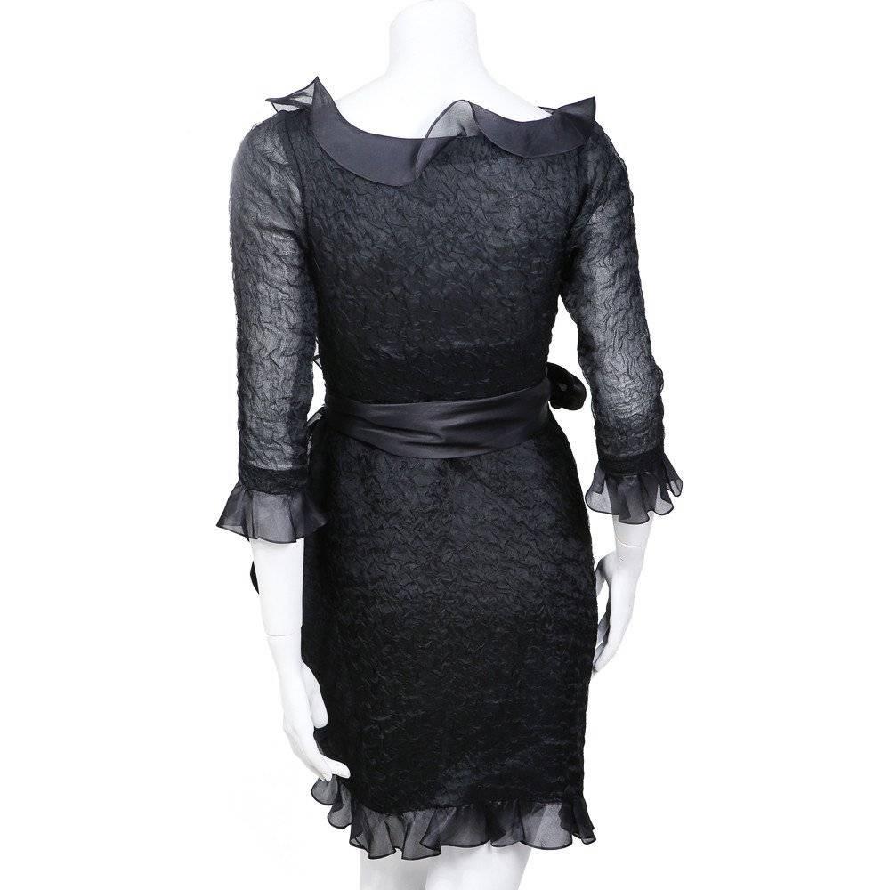 This is black silk chiffon dress by Yves Saint Laurent circa 1980s.  It consists of a crumpled texture chiffon for the body, outlined with smoother chiffon ruffled edges.  Details include half sleeves with ruffled ends, a silk wrap around tie, and a