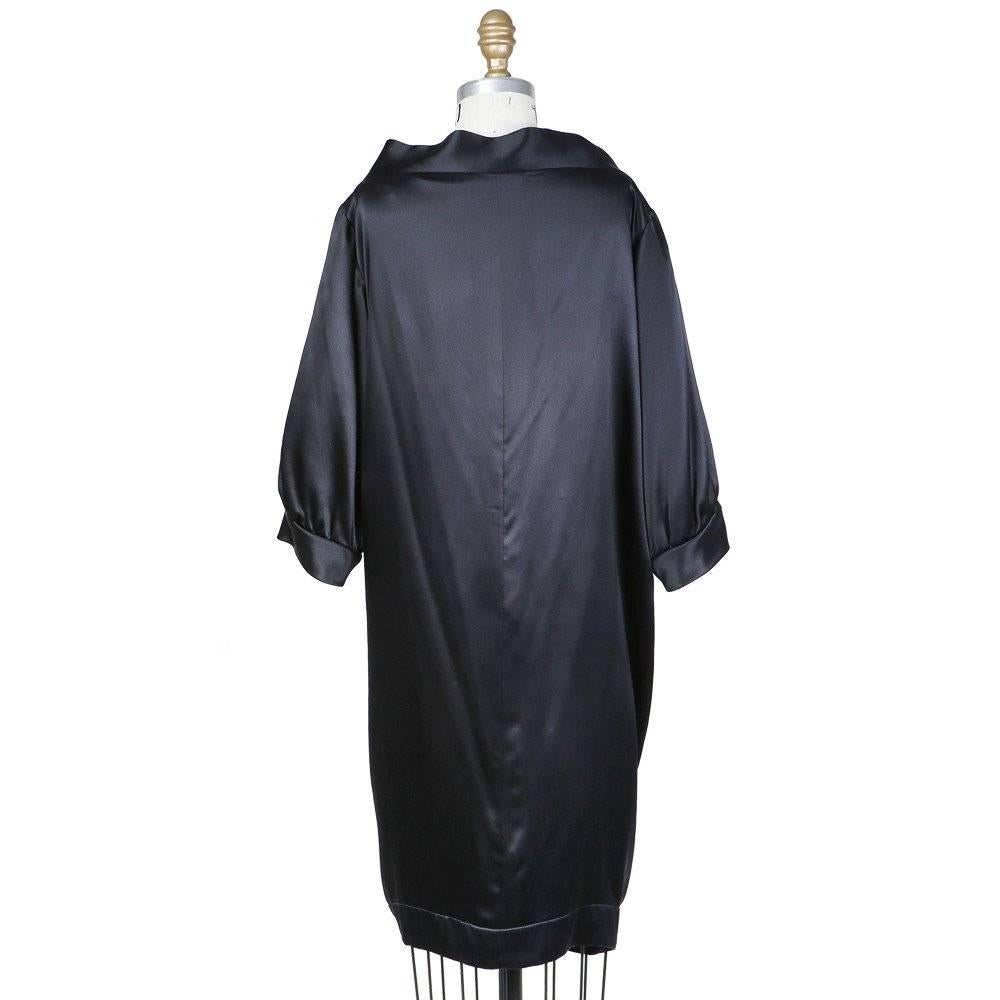 This is an haute couture dress from Yves Saint Laurent. It is a tuxedo style dress made from black satin and features pleated drapes in front and short cuffed sleeves.  Details include internal back panel with wrap around strap under the bust with