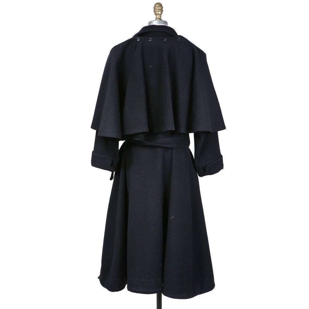 This is a couture black wool coat by Yves Saint Laurent circa 1980s.  It includes a belt around the waist, double breasted button closure, and two front pockets. The capelet is detachable with buttons.  It is satin lined. 