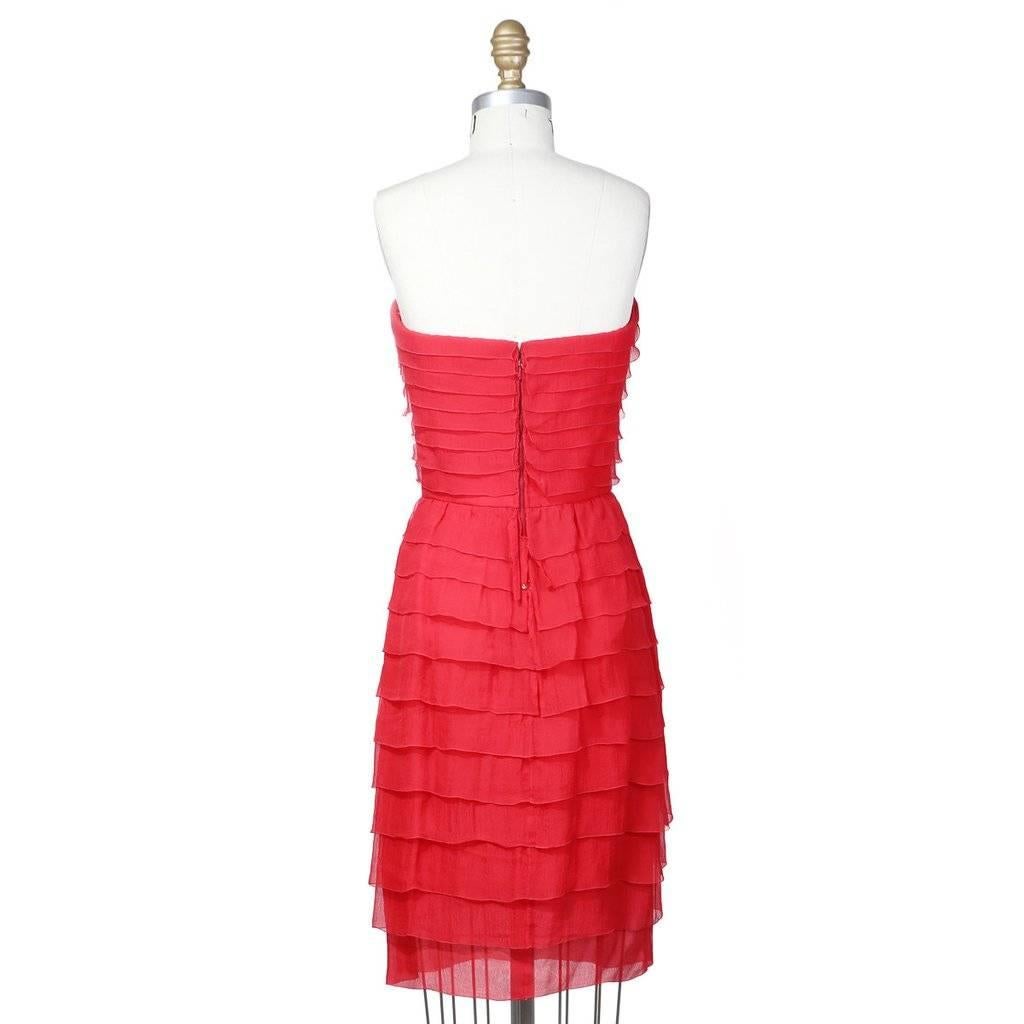 This is a red strapless cocktail dress designed by Oscar De La Renta for Balmain c. 1990s.  It features a sweetheart neckline and layers of fabric similar to a ruffle.  The closure is an invisible internal hook-and-eye at waist and invisible zipper