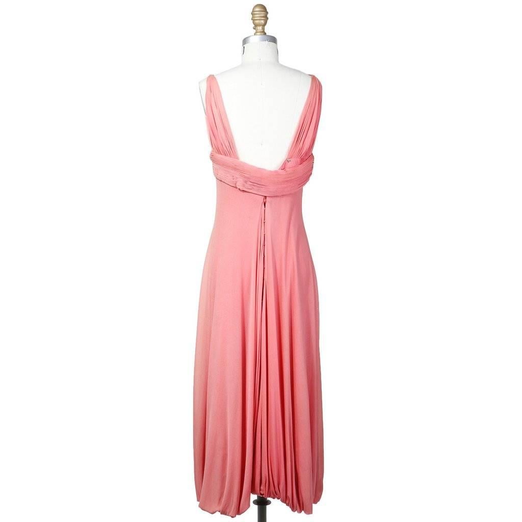 This is a salmon pink chiffon dress by Madame Grès c. 1960s.  It features draped straps that transition into micro pleating around the bust that continues all around the back.  It also has a bubble hem and a structured lining around the bust.  The