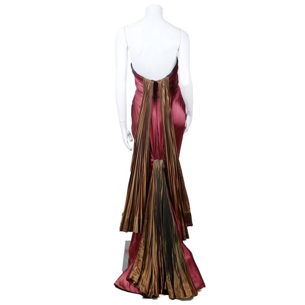 This is a strapless gown by Jean Desses from 1947.  It is done in a burgundy colored silk satin and features a tulip petal neckline and a high-low hem. Other details are the golden green accordion pleated accents in back; one is a train and the