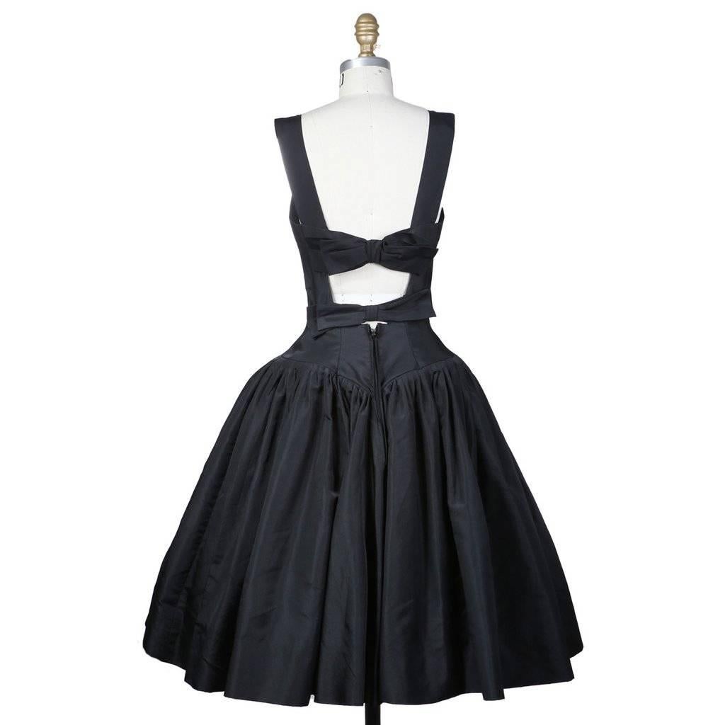 This is a black strapless cocktail dress by Traina Norell circa 1960s.  It includes a  tulle crinoline to create volume under the skirt.  Another featured detail is the two bows in back that act as cross straps and close the back with hook and eye