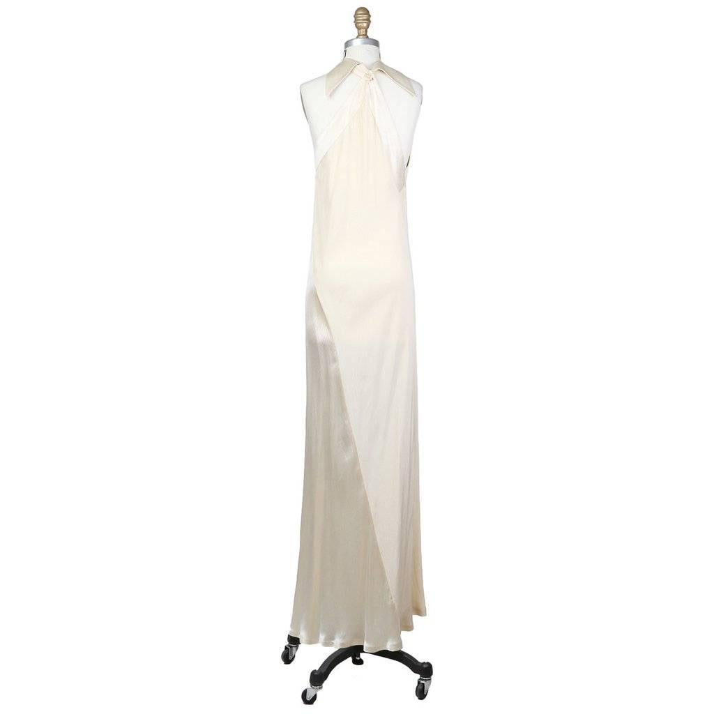 This is an Ossie Clark dress c. late 1960s/early 1970s.  It is a cream colored crepe constructed with an asymmetrical seam to create a subtle drape.  It features a halter neckline with a pointed collar that closes with a pearl button.  Made in