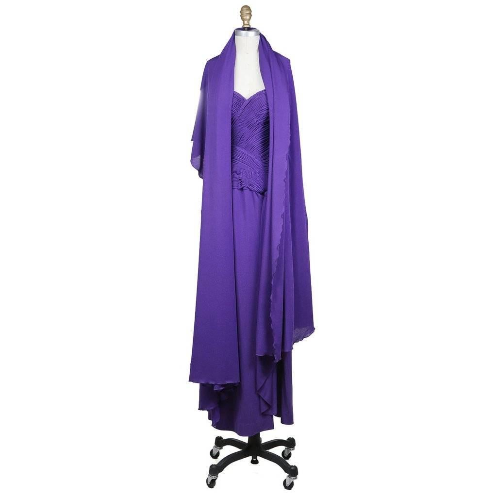 This is purple floor length strapless gown by Loris Azzaro c. 1970s.  It features a ruched and folded bodice that comes down into a knot with a hanging piece of fabric that drapes like a tie.  There is also a side slit and a matching scarf is