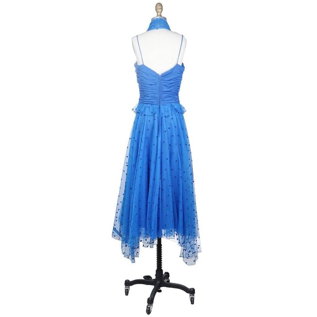 This is a blue dress by Loris Azzaro c. 1970s.  It features a ruched bodice with spaghetti straps and a blue opaque slip covered in two layers of a fine mesh. The top mesh layer is adorned with darker blue felt polka dots.  Other details include a