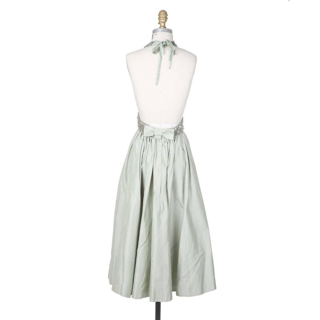 This is a mint colored halter dress by Jacques Fath c. 1980s.  It features a bodice embellished with a combination of beads, sequins, and paillettes.  The tea length skirt is constructed from a subtly textured mint green silk and is lined in satin. 
