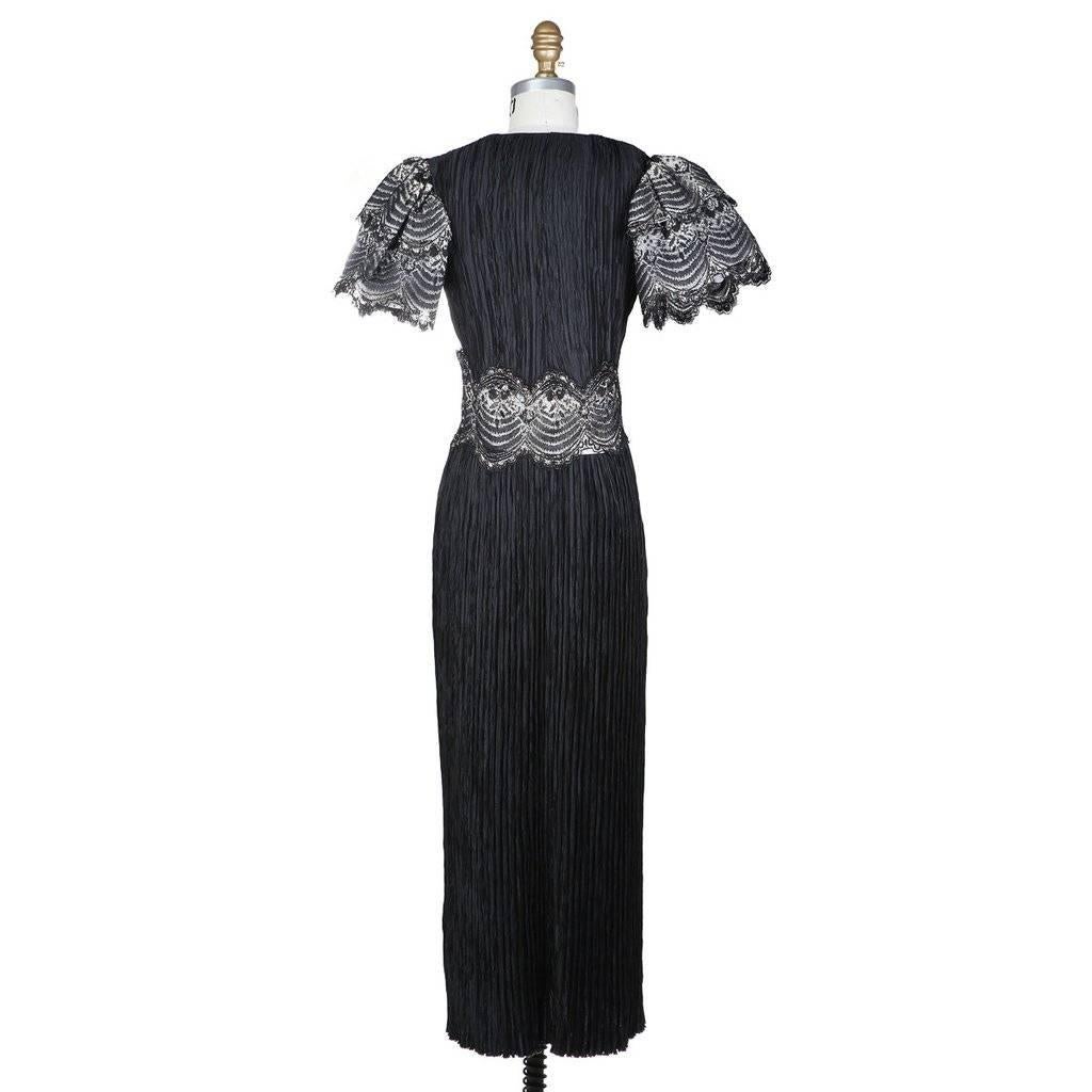 The is a black dress by Mary McFadden c. 1980s.  It features a micro pleated satin creating texture to the fabric.  Other details include tiered butterfly sleeves in lace as well as a lace detail circling the waist. The lace detailing uses gold and