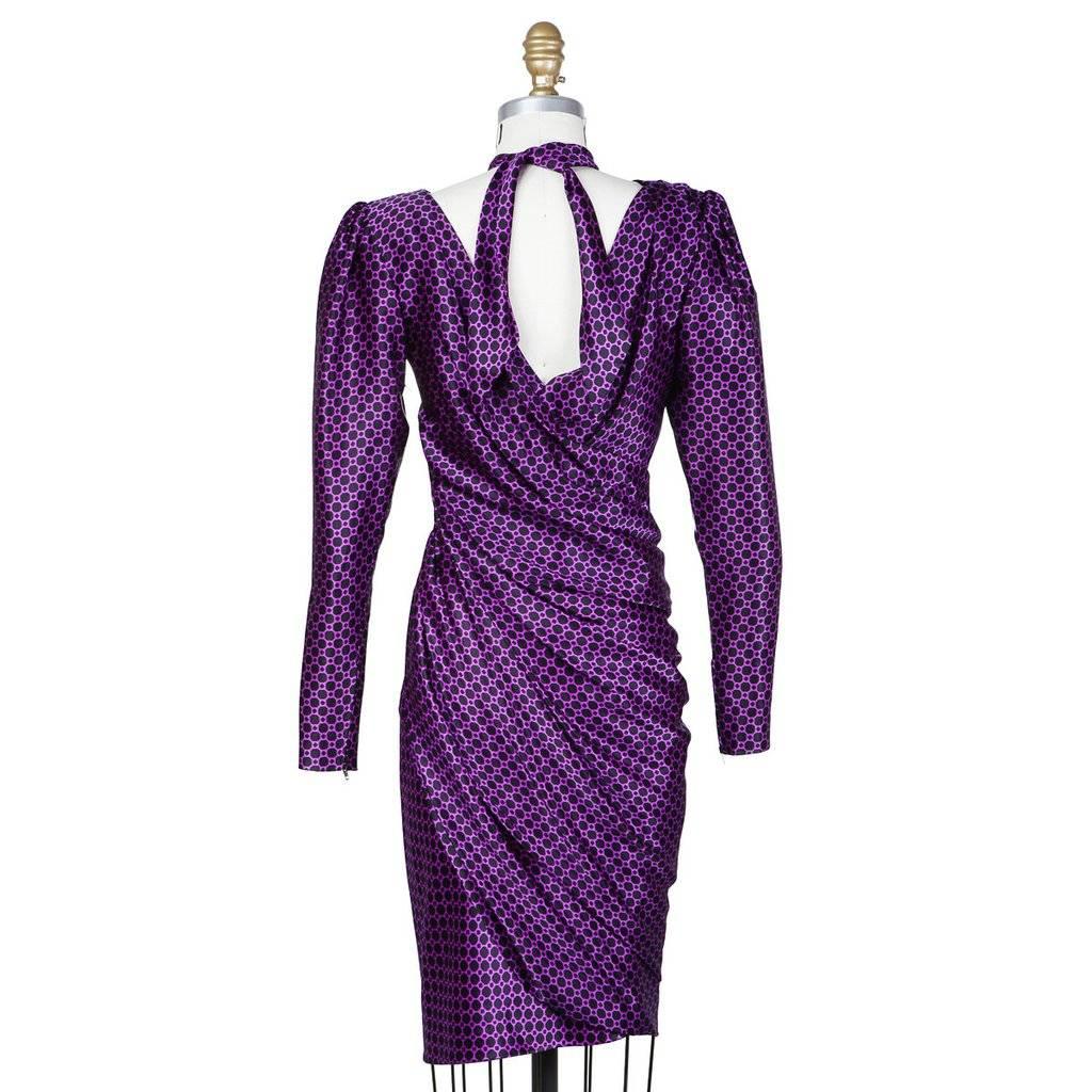 This is a silk cocktail dress from Yves Saint Laurent c. 1980s.  It features a black and purple pattern and gathering at the waist to create a swirling drape around the skirt.  It includes a black chiffon slip and a separate bow to be tied around