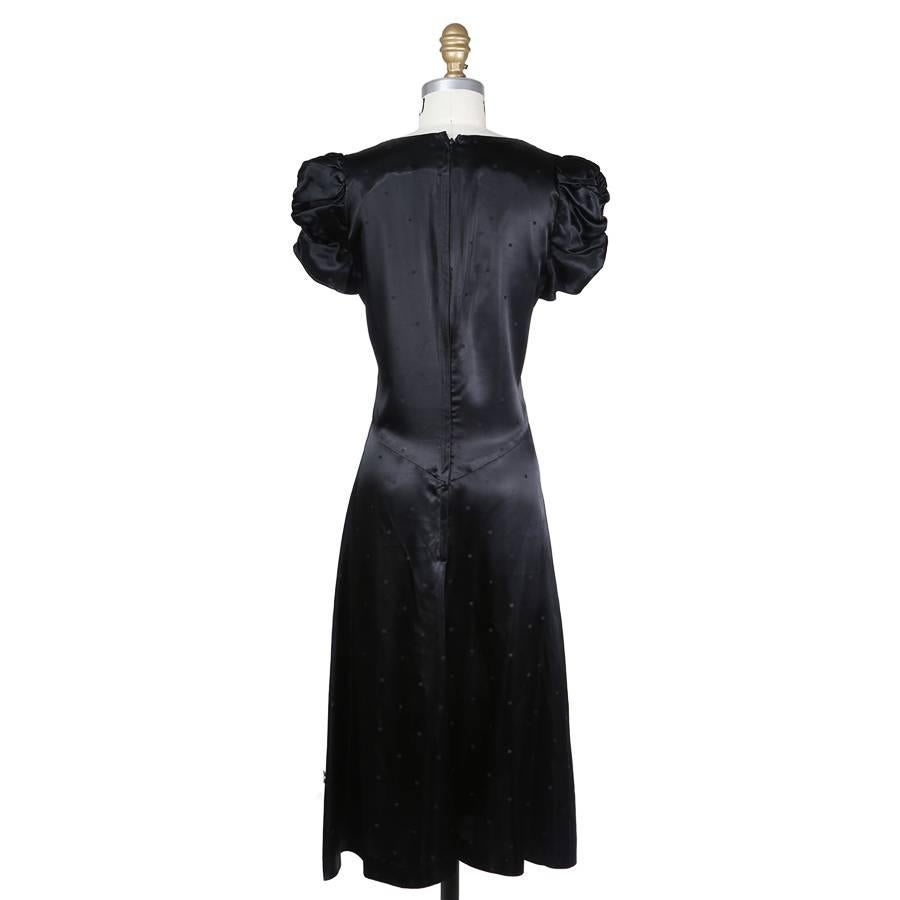 This is a black satin silk dress from Biba c. 1970s.  It has a low V neck line and a flared skirt. Other details include ruched cap sleeves and subtle square polka dots.  