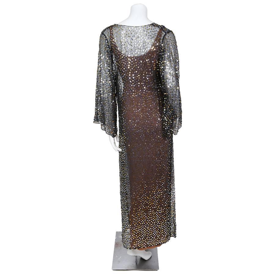 This is a long sleeve dress by Halston c. 1970s.  It’s made from a thin and sheer black chiffon covered in gold and silver paillettes which are connected by a single line of thread to create a subtle zig zag pattern in between.  The dress features a