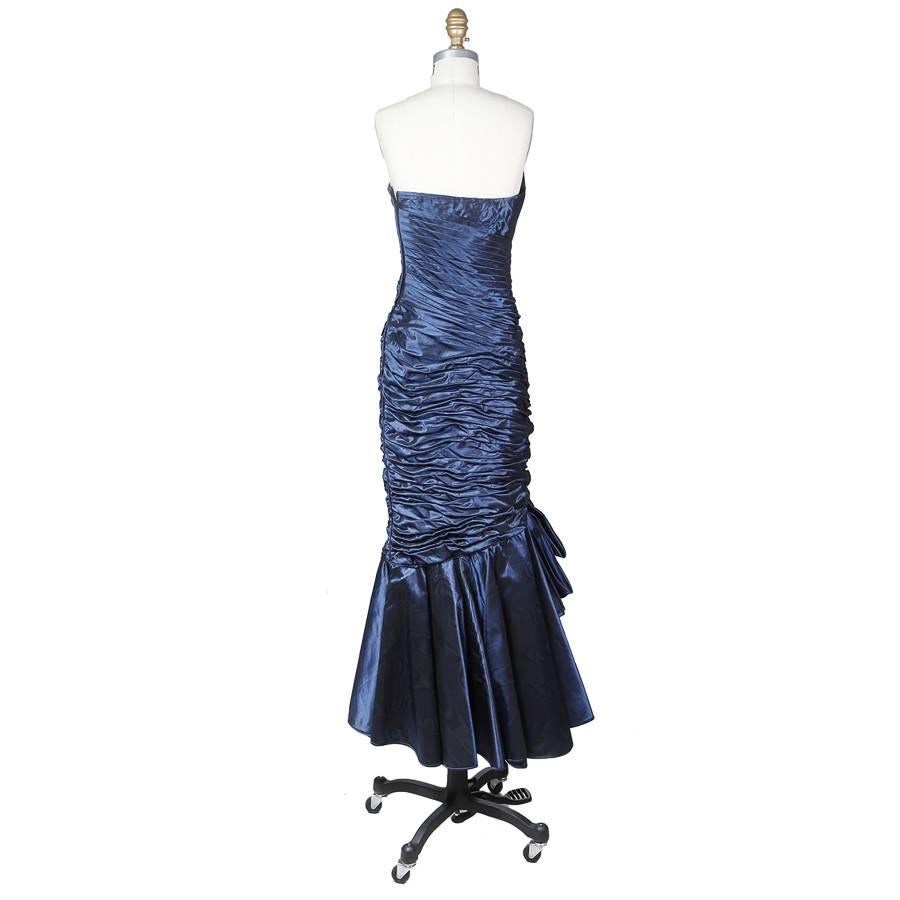 This is a strapless gown by Emmanuel Ungaro c 1980s.  It is made from a navy colored moire fabric which catches the light to give it a shimmer.  It features ruching on the bodice and skirt to create texture and depth.  The neck and hem lines are