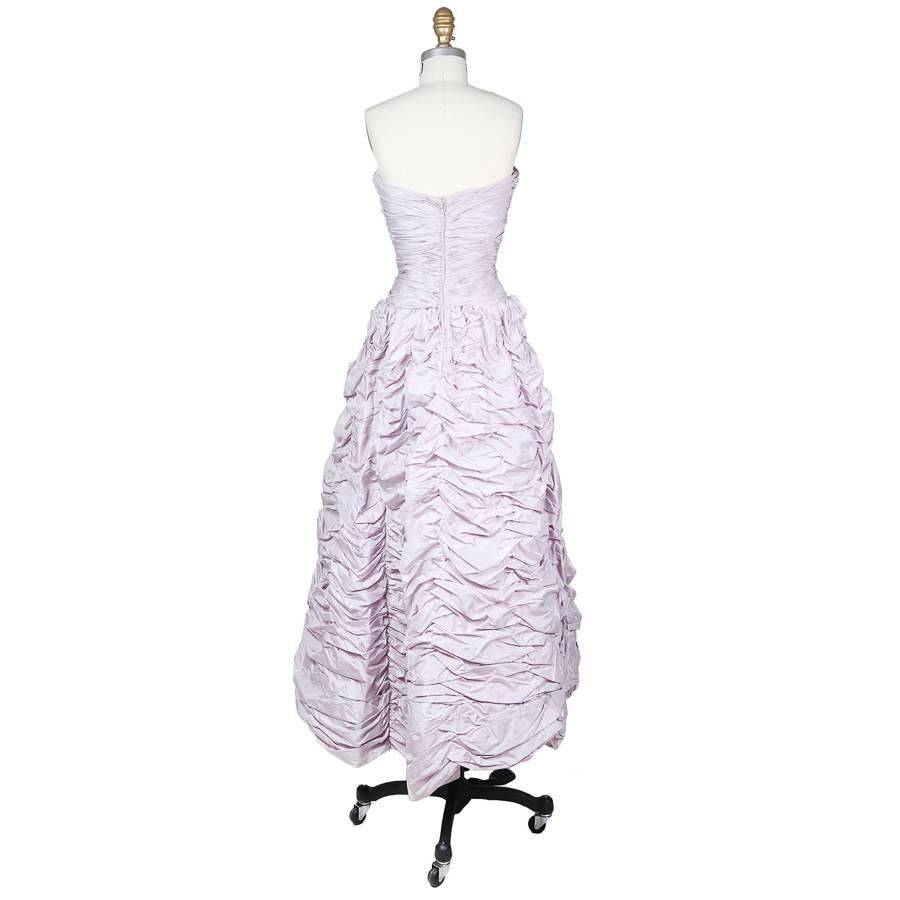 This contemporary strapless gown is by Oscar De La Renta c. 2000s.  It features smaller horizontal ruching in the bodice and the skirt is ruched using big folds of fabric, giving the skirt volume and texture.  The dress includes a structured under