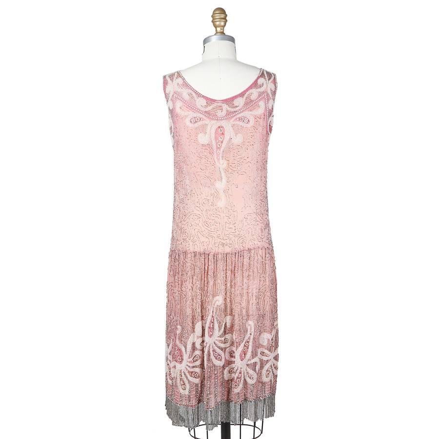 This is a pink chiffon shift dress c. 1930s.  The designer is unknown due to the lack of a tag and its estimated age.  It is covered in a swirling design of beads, dominated by the large swirls of clustered white beads around the neck, down the