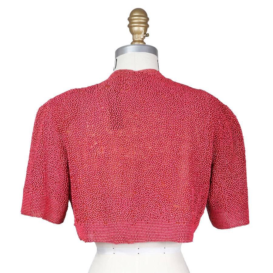 This a cropped jacket c. 1930s.  The designer is unknown due to a lack of tags and its age.  The base fabrics is a rust colored chiffon and it is completely covered in round pink beads.  The shoulder to shoulder measurement is 17” and the sleeve