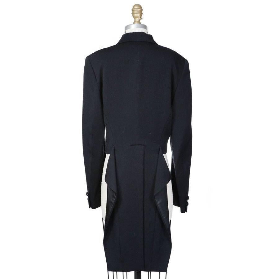 This is a black wool tuxedo jacket by Comme Des Garcons from 1988.  It features a double breasted closure and one chest pocket. The jacket is cropped in front with a coat tail in the back. The coat tail is attached but draped in a way to look as if