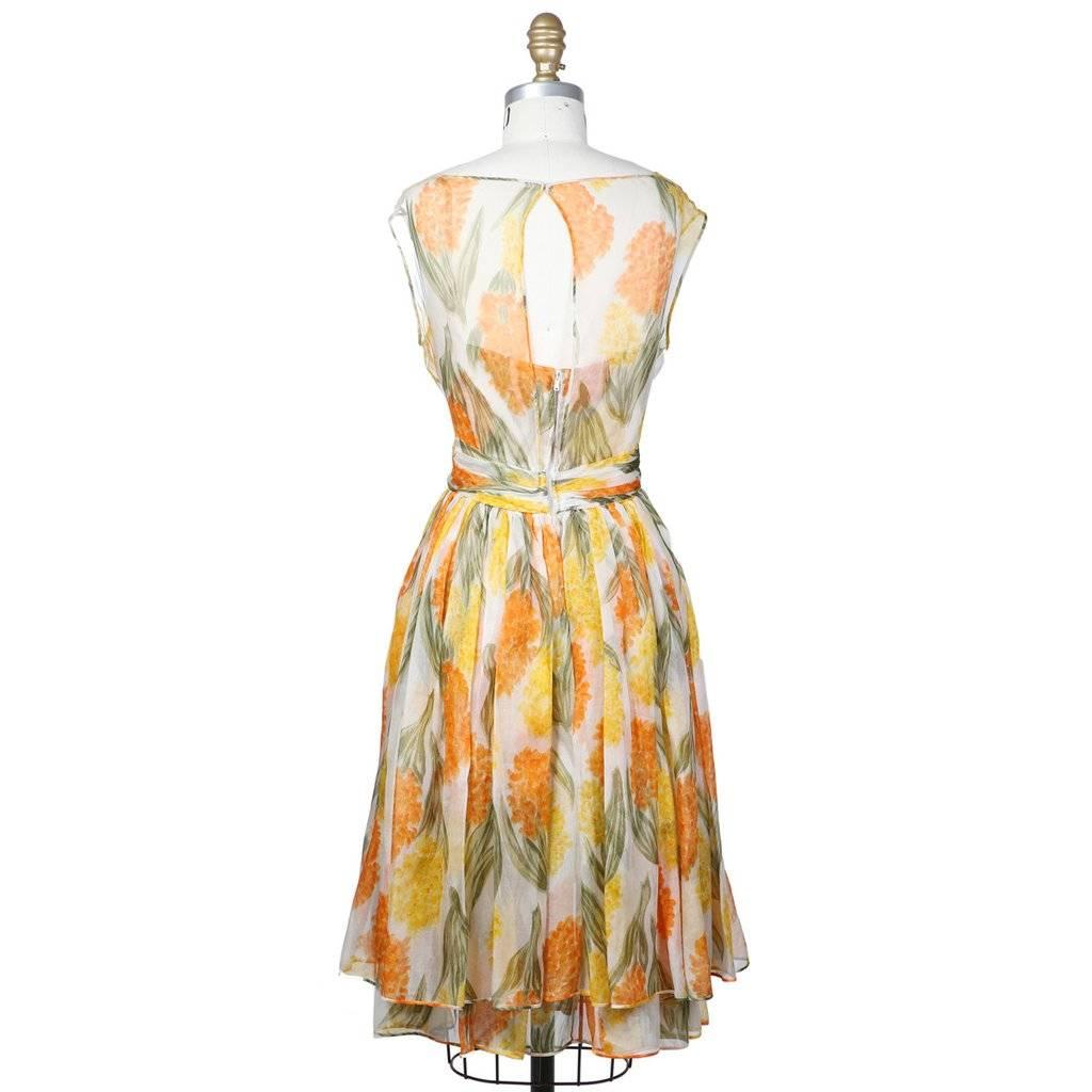 This is a sleeveless floral dress by James Galanos c. 1950s.  It features a double layered A line skirt with an attached wrap for around the waist and lining.  The closure is an invisible zipper down the center back.