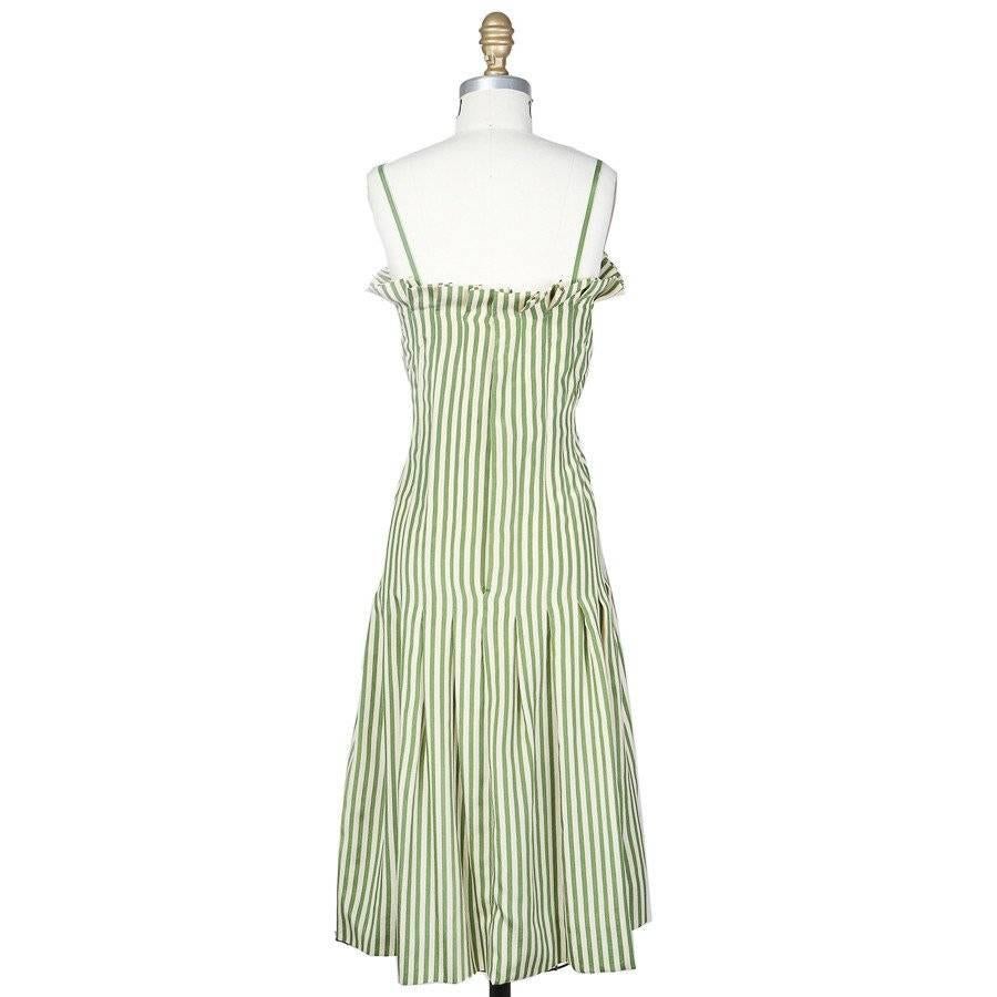 This is a dress by James Galanos c. 1960s.  It features small folded ruffles around the bust line, a pleated skirt, spaghetti straps, and green and cream vertical stripes.  The closure is a zip up the center back
