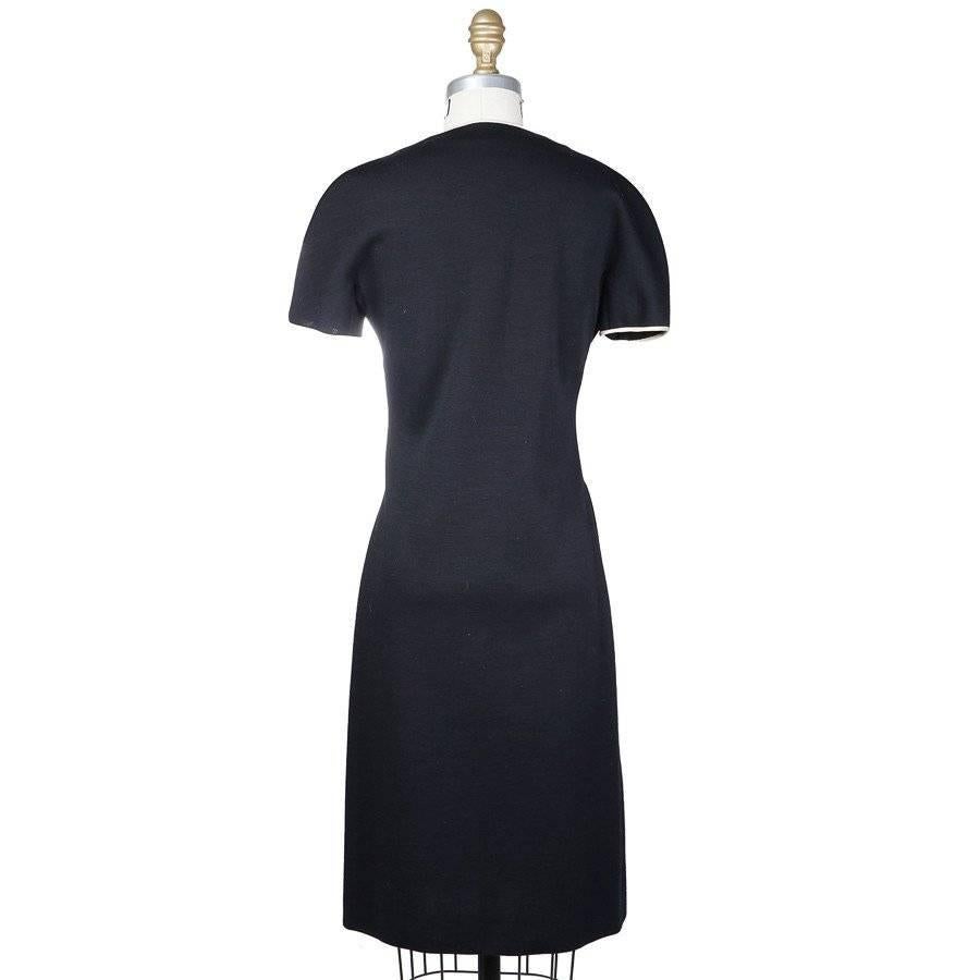 This is a black knit wool dress by James Galanos c. 1980s.  It features white satin trim, an asymmetrical button closure down the front, and short sleeves.  