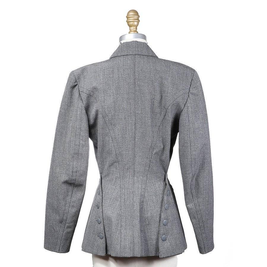 This is a grey blazer by Azzedine Alaia c. 1980s.  It features invisible zippered hip pockets at the sides, double breasted closure with grey metal buttons, and it is silk lined. Another detail to note is the button and flap detail in the back at