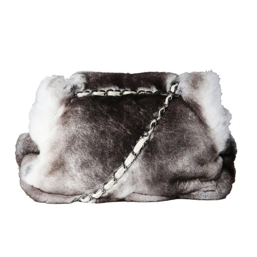 This is a chinchilla flap bag by Chanel from 2003/2004.  It features a zip closure inside hidden by a top flap with a twist lock closure. The interior is cream colored suede, which is woven through the chain link shoulder strap.  The tag is still