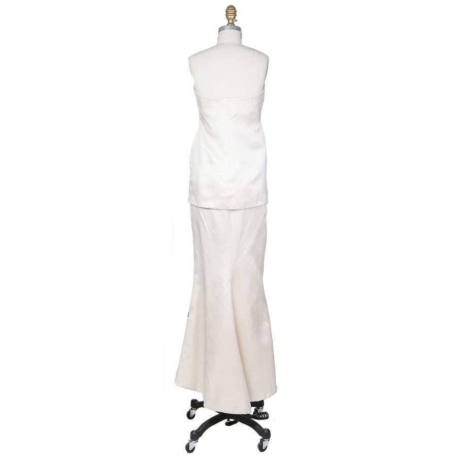 This is a cream colored silk two piece gown by Yves Saint Laurent c 1980s. The top piece features a taffeta rosette in the center of the bust, a sweetheart neckline, and a structured inner bodice.  The skirt is a mermaid cut.  Both pieces close with