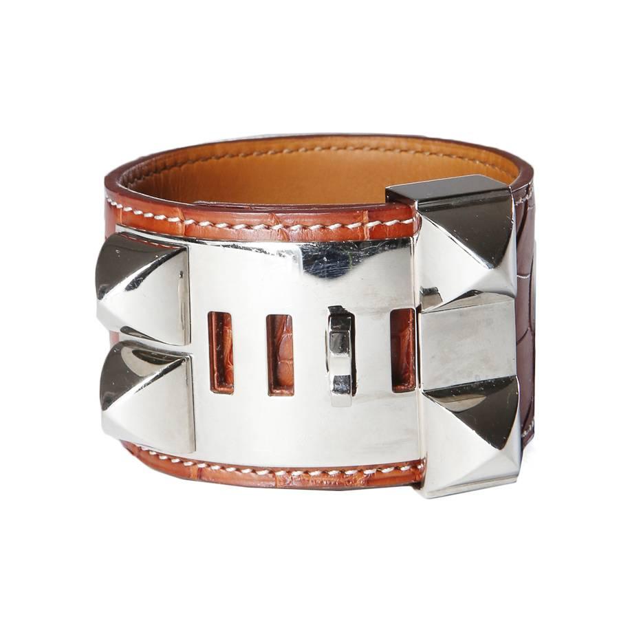 This is a tan crocodile cuff by Hermes from 2012.  It features contrast stitching and pyramid studded plates.  It is adjustable by 4 notch sizes, 6.5" circumference at its largest and 5.5" circumference at its smallest.  The width of the