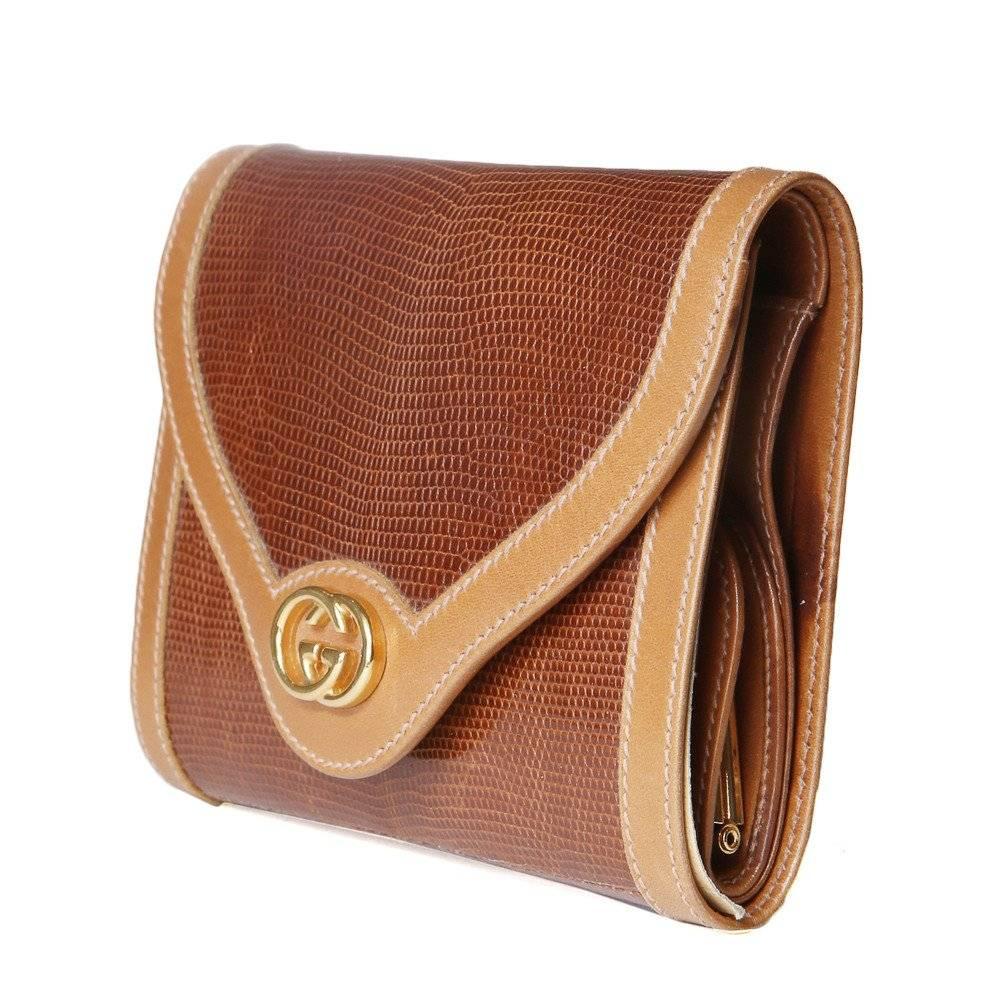 This is a tan lizard wallet from Gucci c. 1980s.  It features multiple pockets including a long money slit, an attached traditional coin pouch, a plastic card holder, gold hardware, leather trim, and a gold logo on top of a snap closure.
Length is