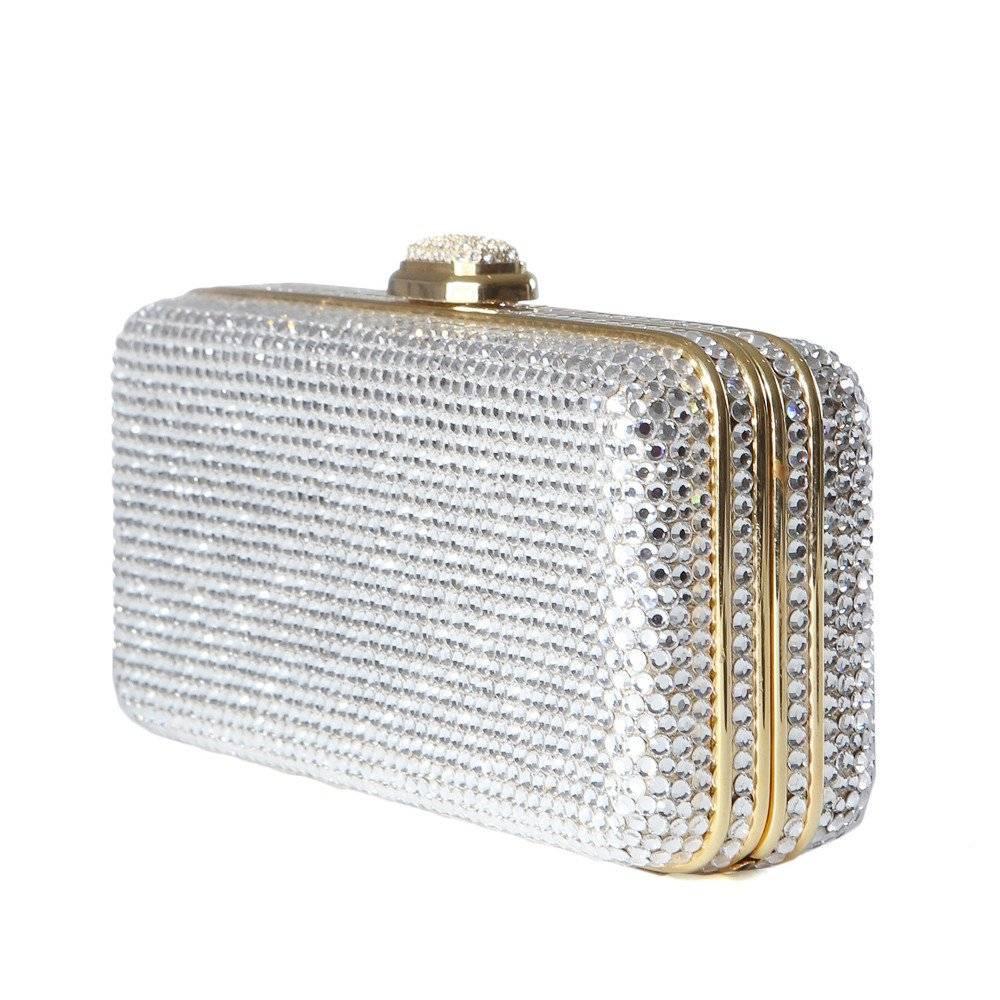 This is a rectangular clutch by Judith Lieber c. 2000s.  It is covered in crystals and features a gold interior, pocket mirror with satchel, and has an attached 40" chain to convert the clutch into a shoulder bag. The clutch itself is