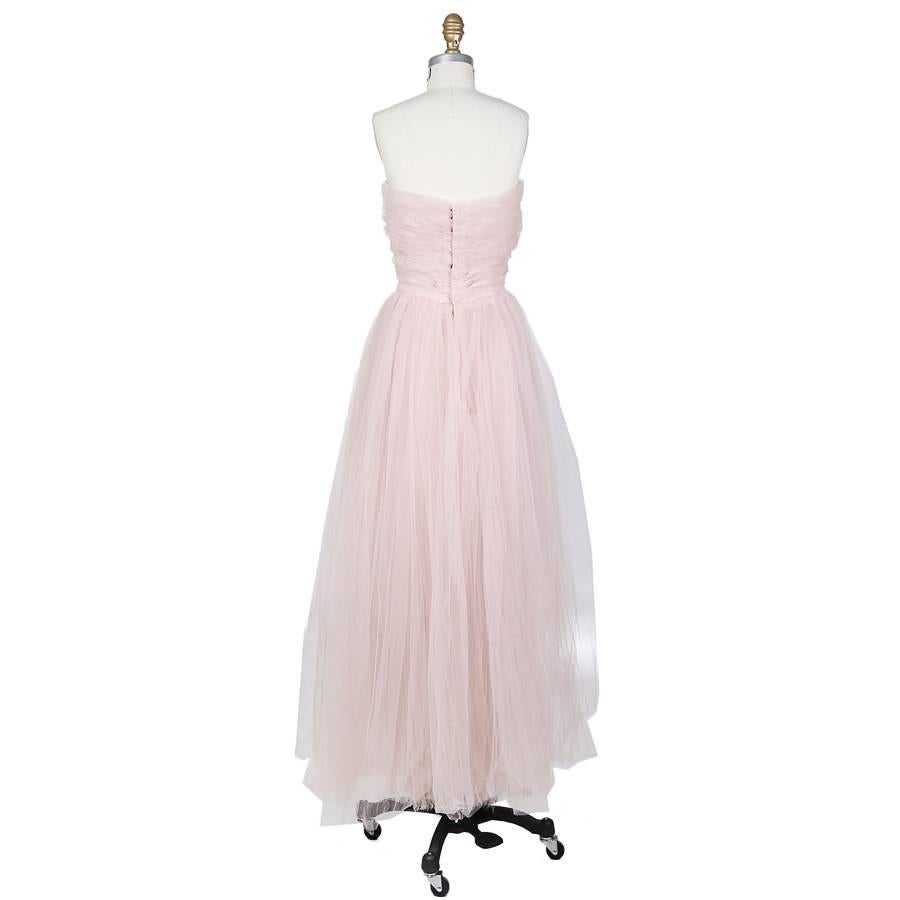 This is a strapless gown by Christian Dior New York c. 1950s.  It is made of a blush pink tulle and includes an inner corset.  The closure is hook and eye with snaps.  