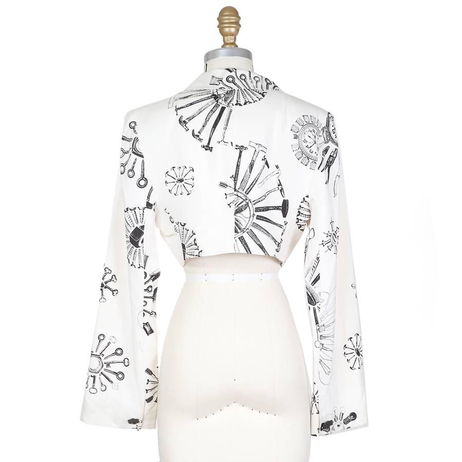 This is a bolero jacket by Todd Oldham from spring 1994.  It features long sleeves and a black and white circular ray pattern and a curved hem.  
15" shoulder to shoulder
23" long sleeves