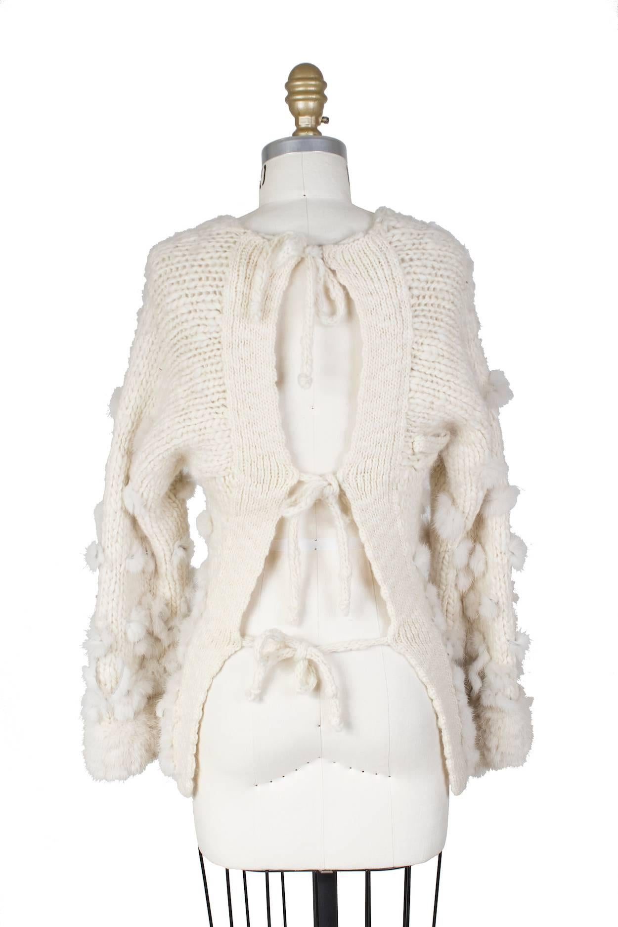 This is a cream colored wool sweater by Jean Paul Gaultier c. 1990s.  It features mink fur accents and bell sleeves.  The back is open with 3 tie closures.