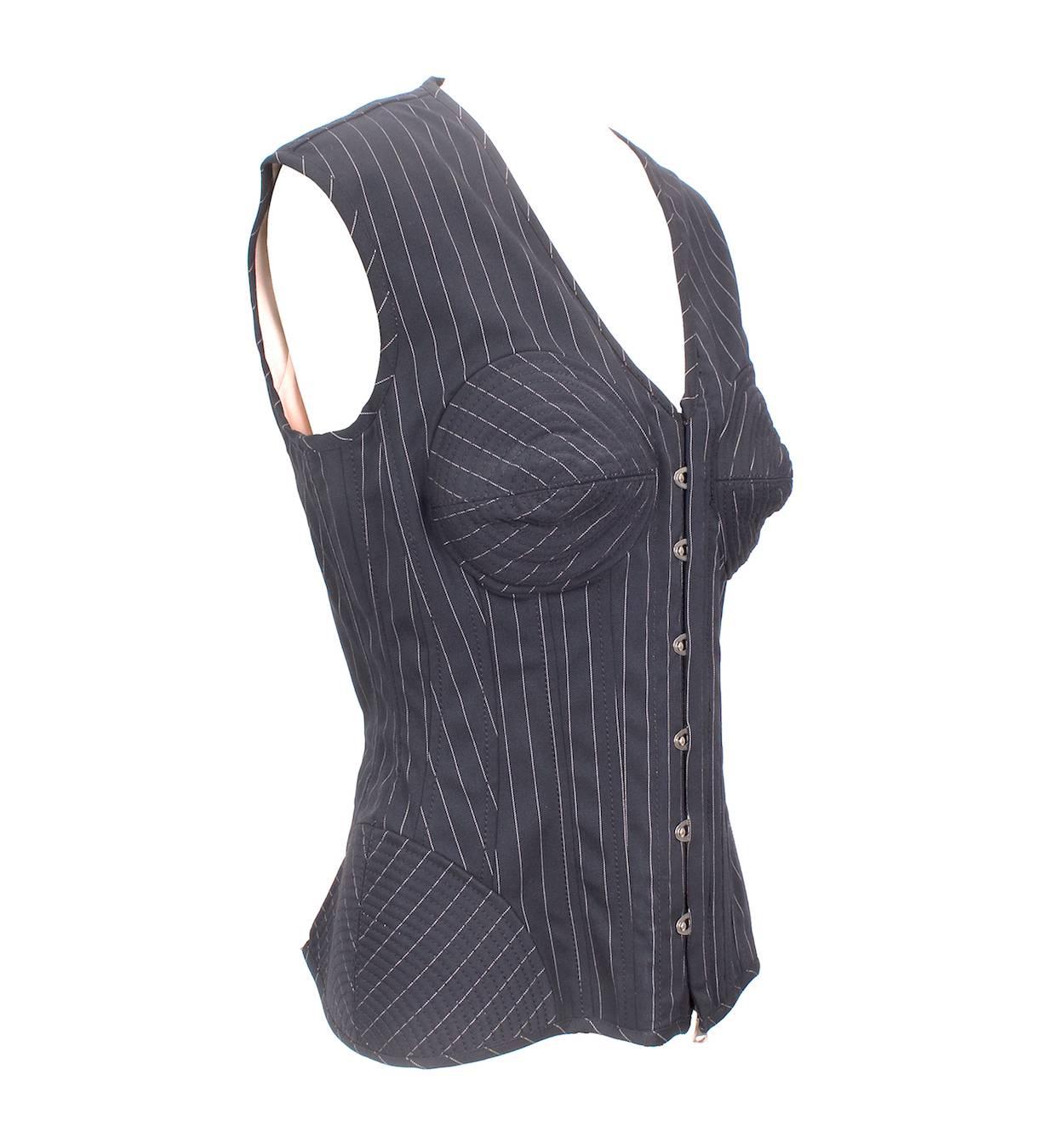 This is a navy pinstripe vest by Jean Paul Gaultier c. late 1980s.  It features a cone bra and structured corset details around the hip.  The closure is latch clasps over a front zipper.  The back is a blush pink stretch material with a cinch strap.