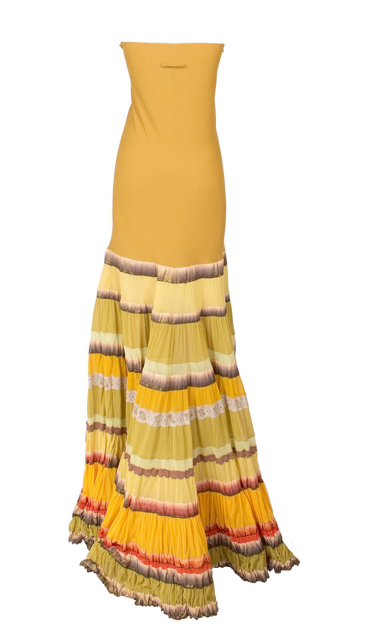This is a tube top dress by Jean Paul Gaultier from Spring 2005.  The body is a mustard yellow stretch material and the skirt has rows of ruffles and pleats.  