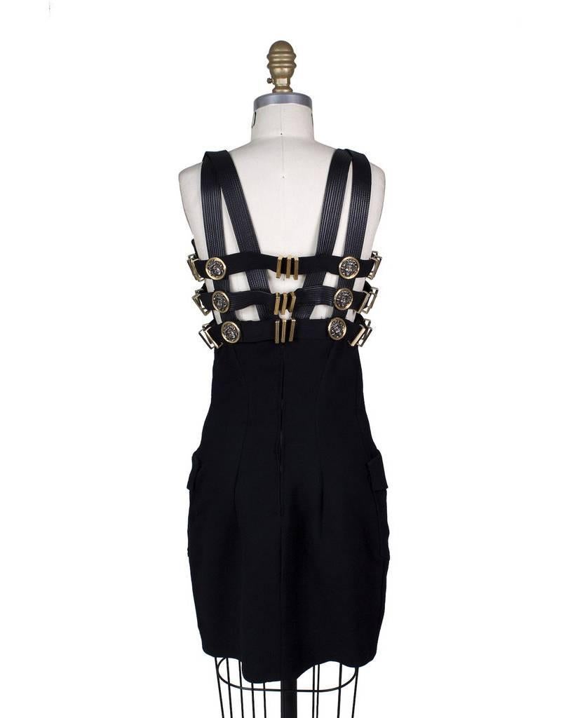 This is a dress by Gianni Versace for his fall 1992 bondage collection.  It is made of wool and silk and features a multi strap closure around bust with gold versace medusa medallions.  