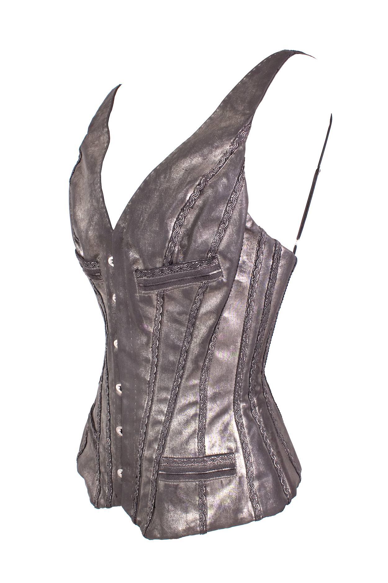 This is a corset vest by Jean Paul Gaultier c. 1990s.  It is made of a shiny metallic leather with braiding trim details and lace up in the back.  The front has a multiple latch closure.