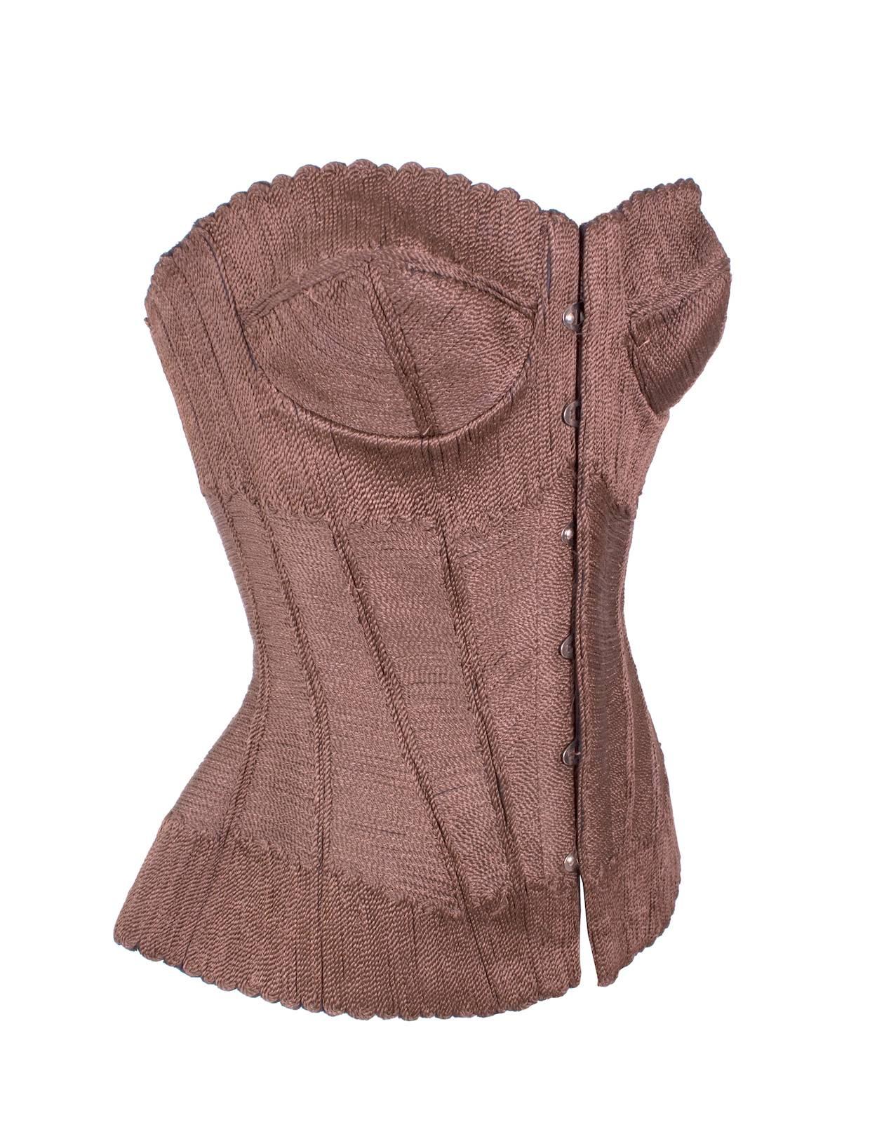 This is a fitted bustier by Jean Paul Gaultier c. 1990s.  It is covered in brown braided threads to give it a woven texture.  It has latch clasp closures in the front and shoestring lace up in the back.  Lined in black silk satin.