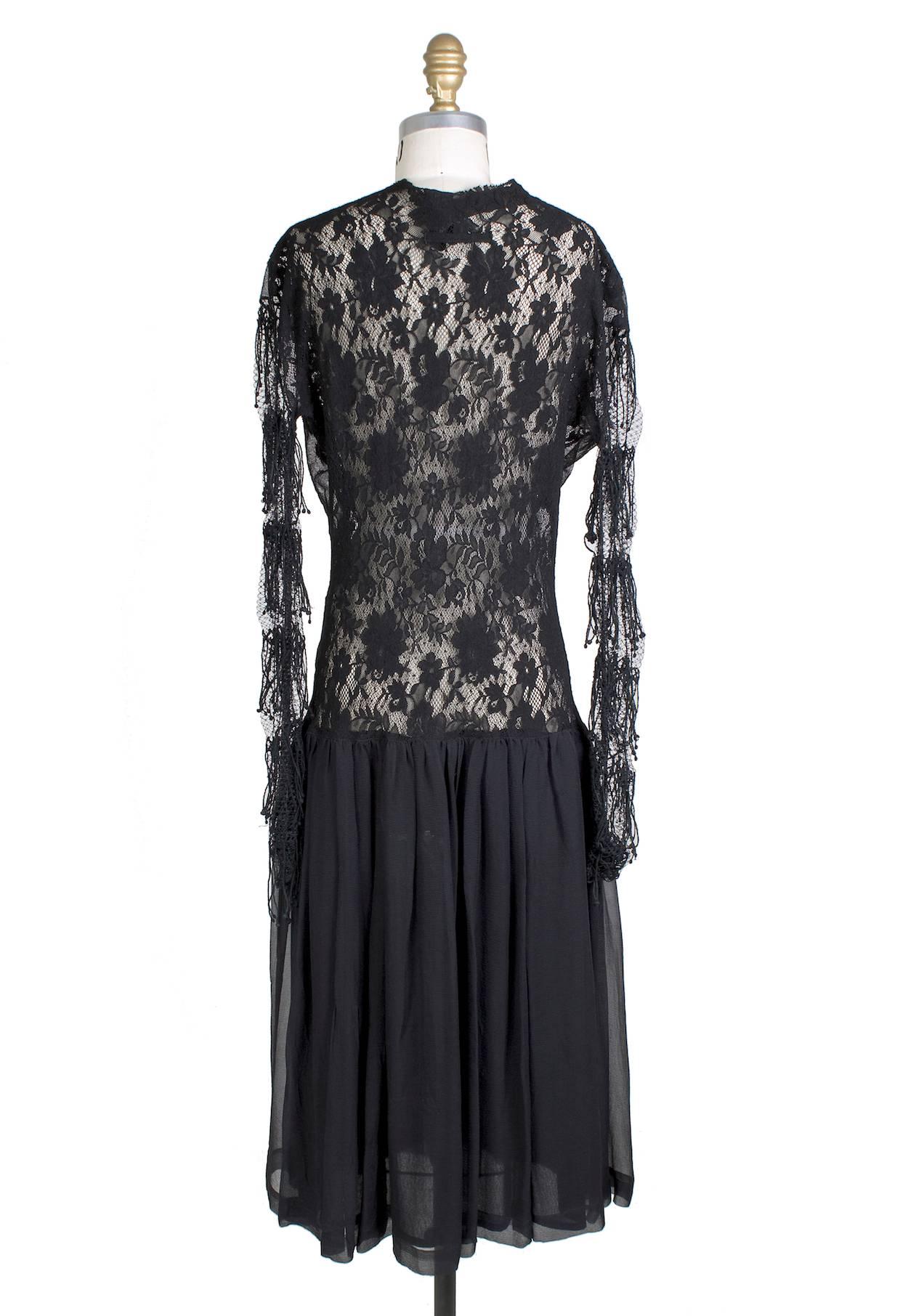 This is a black lace dress by Jean Paul Gaultier c. 1990s.  It features long tiered lace sleeves with scalloped lace front and a sheer silk skirt.  The closure is buttons down the front.  